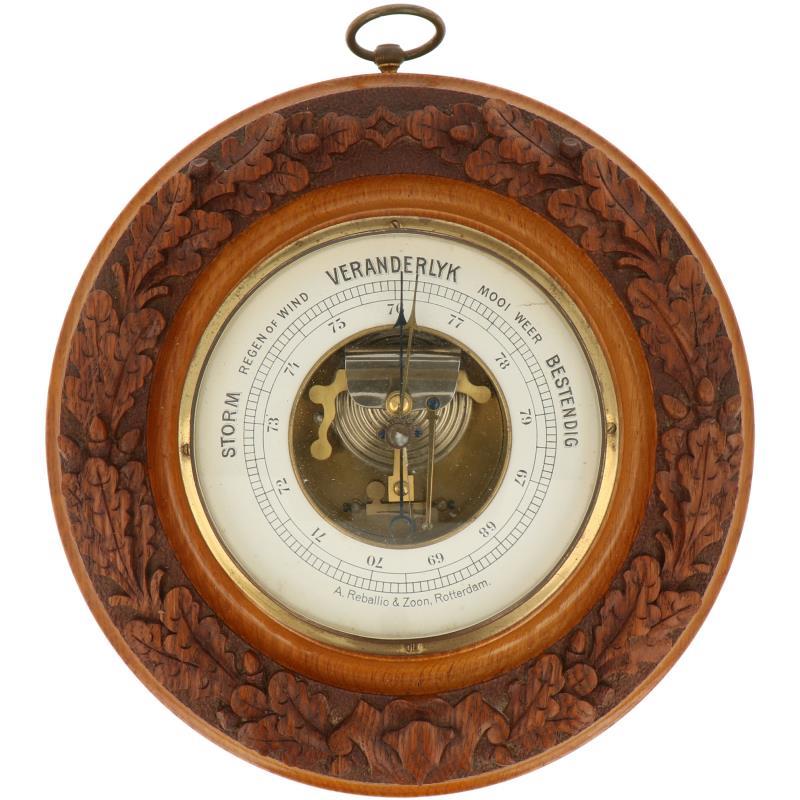 Een ronde barometer met snijwerk van eikenbladeren. Adres: A. Reballio & Zoon, Rotterdam. Ca. 1930.