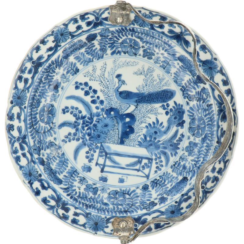 Een porseleinen bord met floraal decor van onder andere een pauw, gemerkt met een bloem. China, Kangxi.