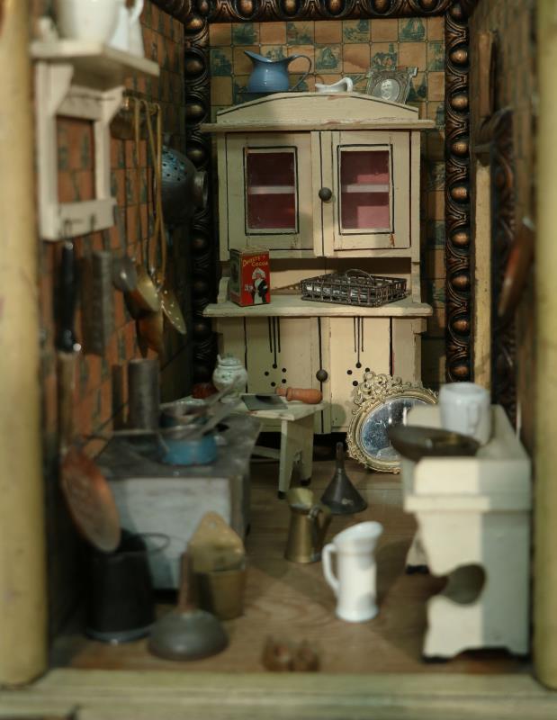 Een zachthouten poppenhuis bestaande uit drie kamers waaronder een kinderkamer, salon en keuken. Circa 1900.