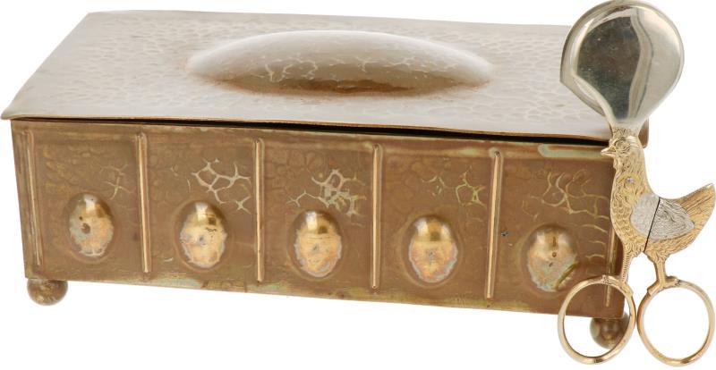 Een gehamerd koperen tabaksdoos met daarbij een eierknipper.