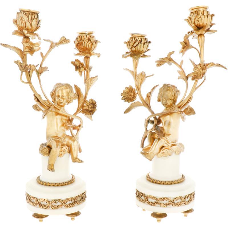Een paar verguld bronzen kandelaren van putti met bloemenrank op wit marmeren basement. 