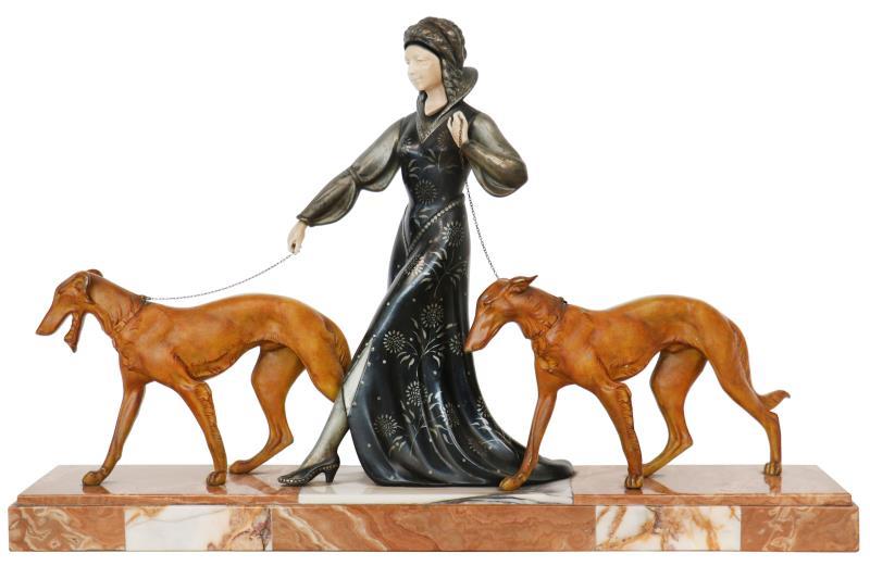 Een koudbeschilderde ZAMAC beeldengroep van een elegante vrouw met twee hazewindhonden op een marmeren plint. Handen en gezichtje zijn mogelijk van ivoor. 
