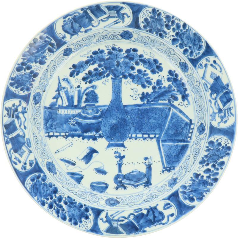 Een porseleinen schotel met antiquiteiten in landschapsdecor, gemerkt met ruit. China, 18e eeuw.