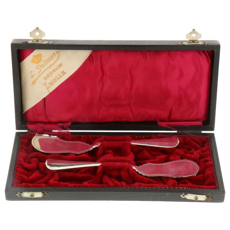 (2) Delige set botermesjes met gegraveerde versieringen in originele etui zilver.