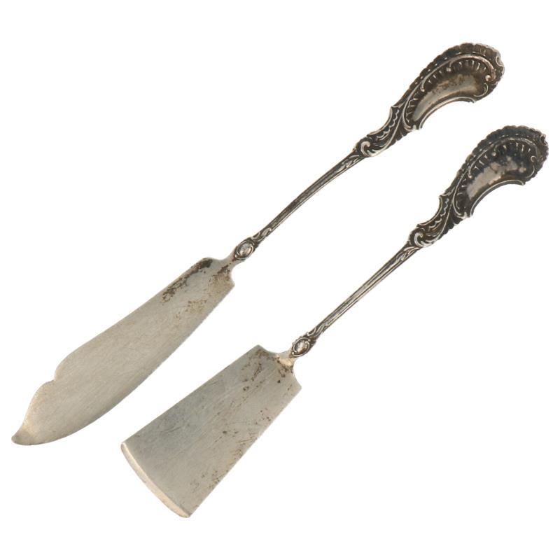 (2) Delige set met kaasschep en botermes met fraaie rocaille versiering zilver.