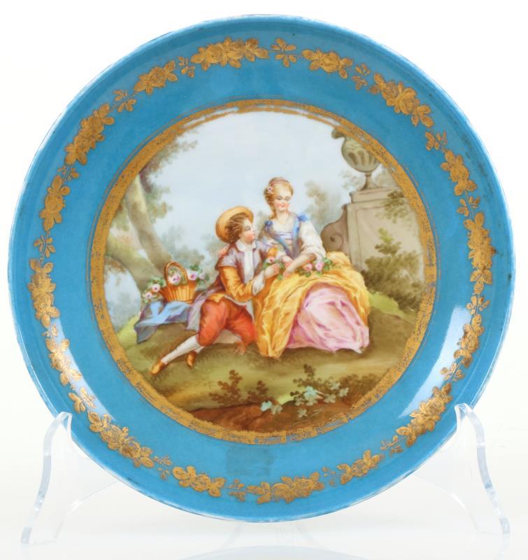 Een porseleinen bord met blauw fond en in het centrum een romantische scene, gemerkt Sévres. Frankrijk, eind 19e eeuw.