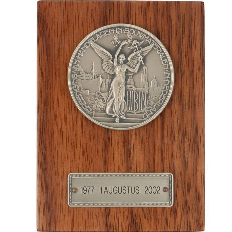 Nederland. Houten plaquette met gemonteerde zilveren penning van de Vereniging van bouwmaterialenhandelaren. (Afbeelding verkleind).