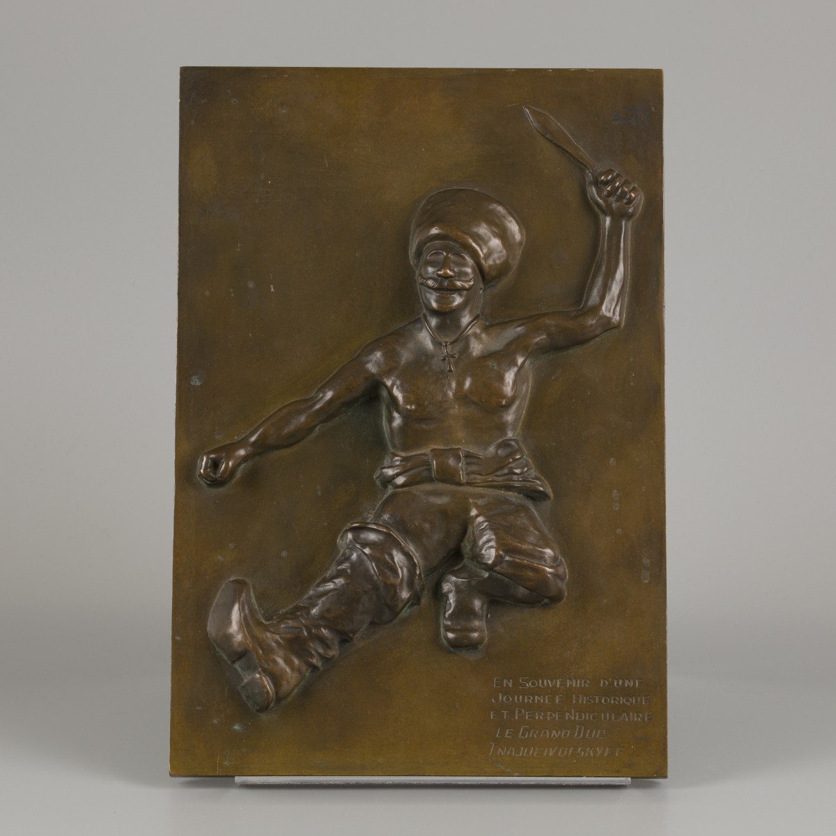 Een bronzen plaquette met voorstelling van een dansende kozak.