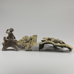 Een paar gegoten bronzen vuurbokken daarbij een restant van een klok met putto, allen 19e eeuw.