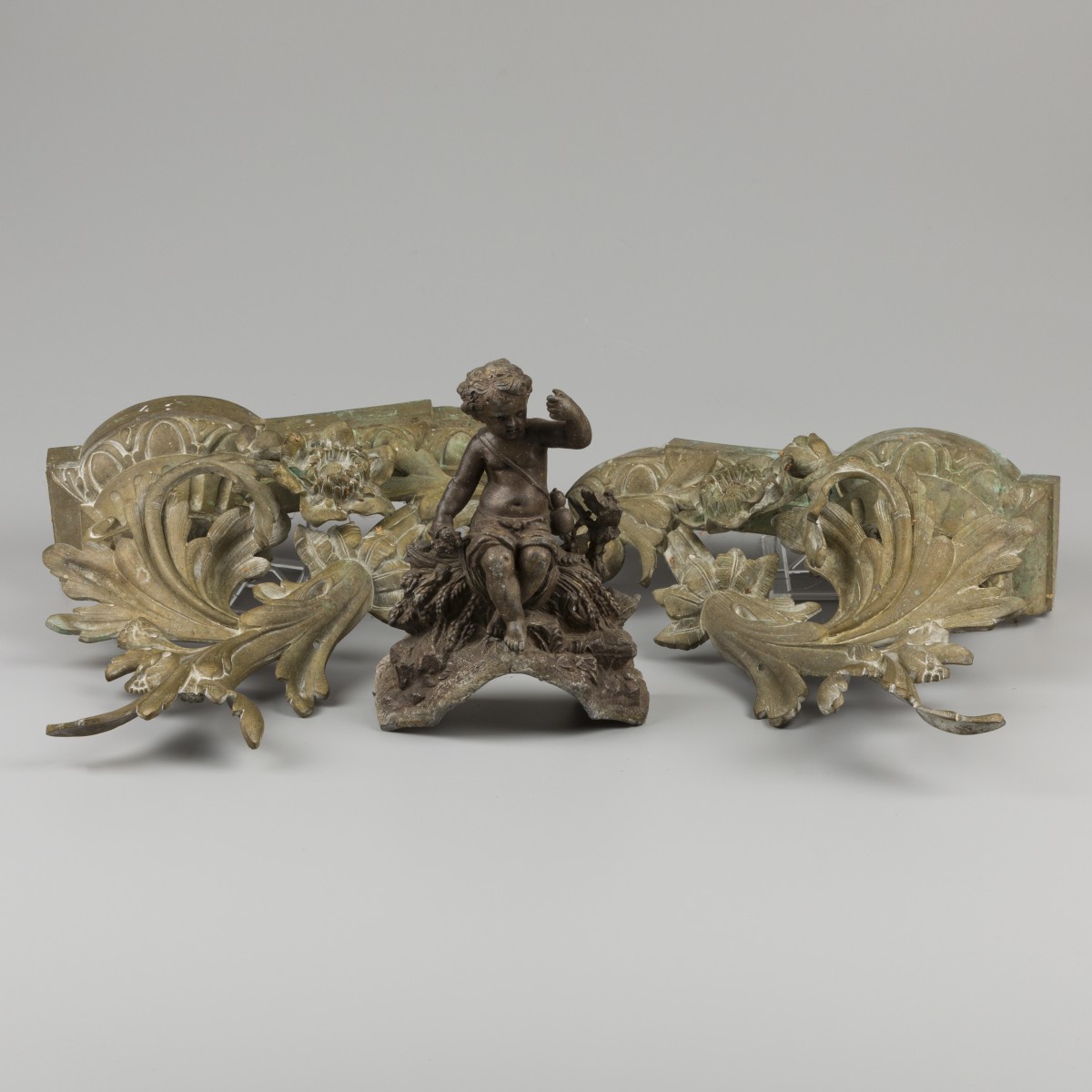 Een paar gegoten bronzen vuurbokken daarbij een restant van een klok met putto, allen 19e eeuw.