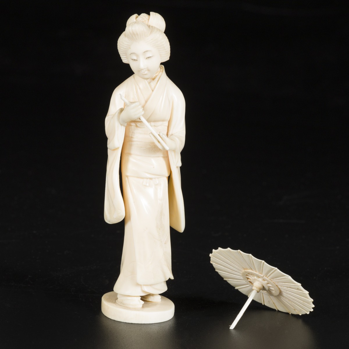Een ivoren sculptuur in de vorm van een dame met parasol. Japan, einde Meji-periode.