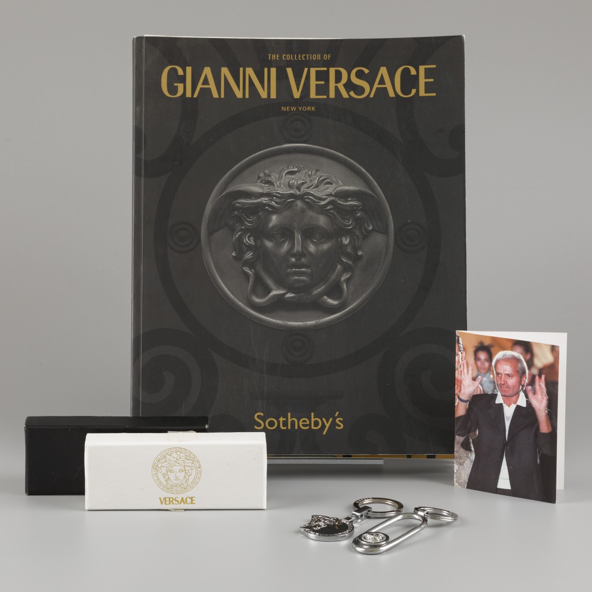 Een lot bestaande uit twee sleutelhangers, een bidprentje van Gianni Versace en de catalogus van de collectie van Gianni Versace (Sotheby's Mei 2005).