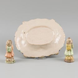 Een majolica schotel met voorstelling van putti die spelen met een geit, daarbij twee kaarsenhoudertjes, 20e eeuw.