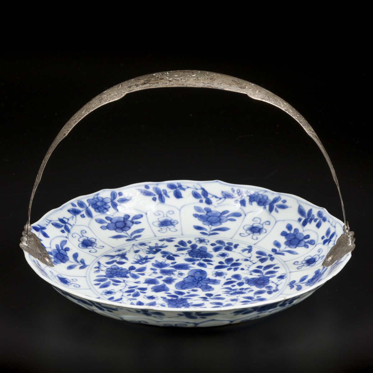 Een porseleinen bord met bladperk decor buitenrand en floraalinterieur Chinees Kangxi met zilveren beugel 19e eeuw.