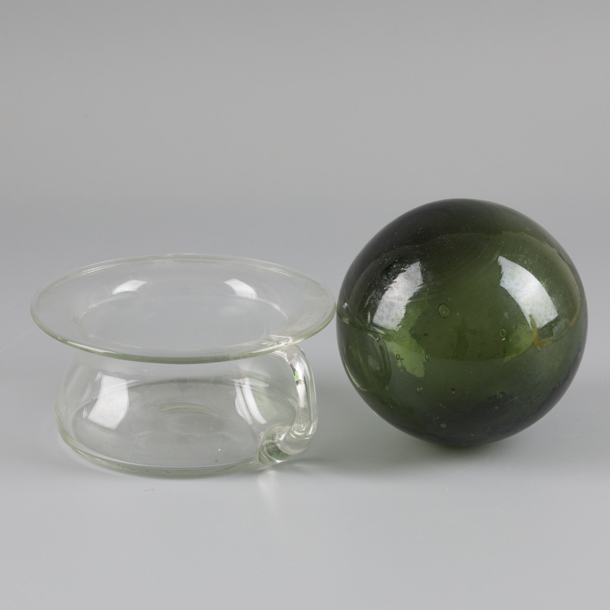 Een transparant glazen po met daarbij een groen glazen bol, 20e eeuw. 